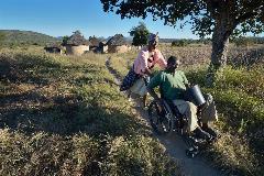 Nhaume Makavire pushes her husband, Henry Gwese, on their farm in Charumengwe, Zimbabwe. Gwese's legs were paralyzed by cerebral malaria, yet he and his wife continue farming. He uses an appropriately designed and fitted wheelchair provided by the Jairos Jiri Association with support from CBM-US.